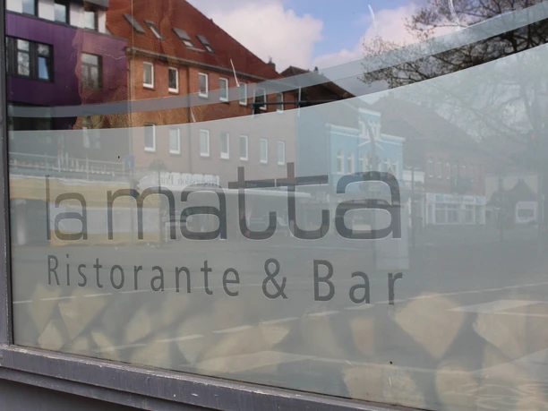 The photo shows the restaurant "La Matta" in a street scene with reflected buildings in the window.