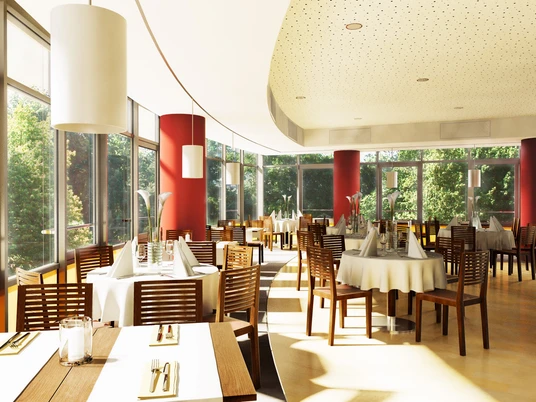 Restaurant Helles, modernes Restaurant mit Holzmöbeln und großen Fenstern, durch die grüner Wald sichtbar ist.