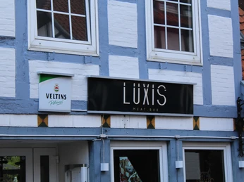 Luxis Meatbar Luxis Meatbar in einem weißen Fachwerkhaus mit grauen Akzenten und einem Veltins Schild.