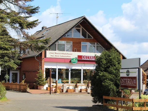 Osteria Restaurant Osteria im Landhausstil mit großer Fensterfront und Außensitzbereich bei sonnigem Wetter.