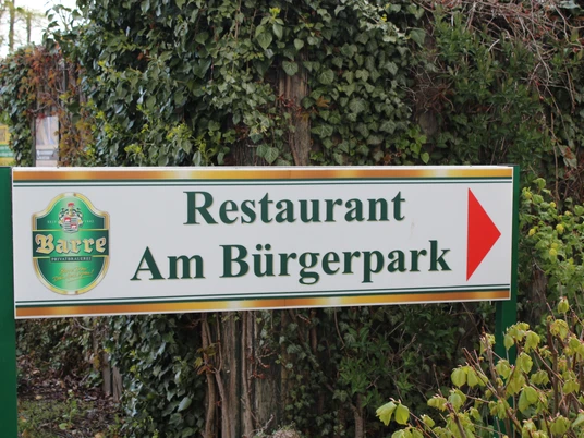 Restaurant am Bürgerpark Schild des Restaurants Am Bürgerpark mit Logo, umgeben von üppigem Grün und blühenden Pflanzen.Restaurant Am Bürgerpark sign with logo, surrounded by lush greenery and flowering plants.Restaurant Am Bürgerpark-skilt med logo, omgivet af frodigt grønt og blomstrende planter.Restaurant Am Bürgerpark met logo, omringd door weelderig groen en bloeiende planten.