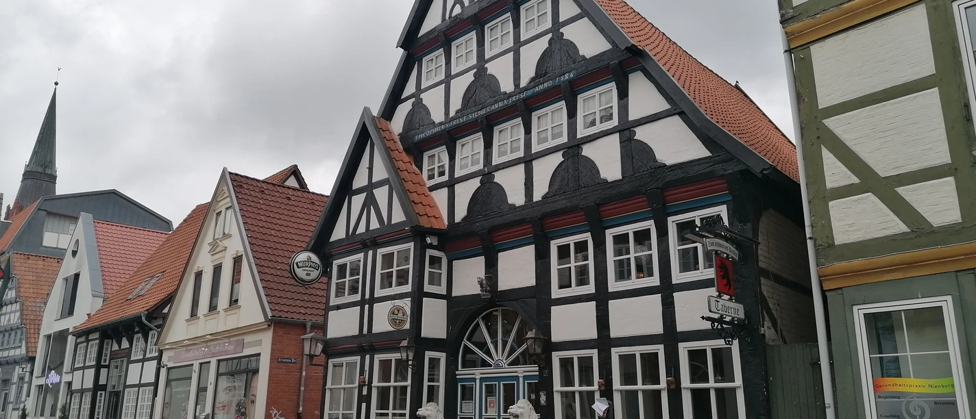 Half-timbered house with red roof tiles and two stone lions at the entrance gate, flanked by neighboring houses.