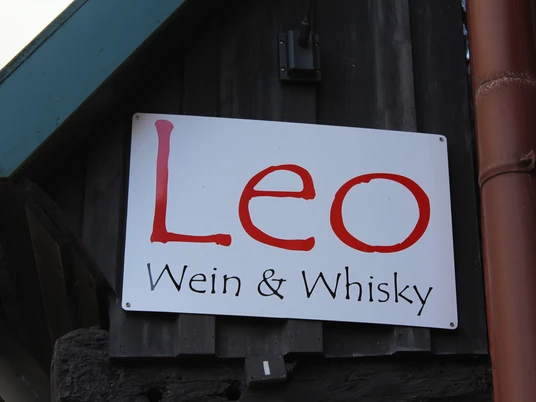 Ein hölzernes Wandschild mit der Aufschrift "Leo Wein & Whisky" in großer roter Schrift.