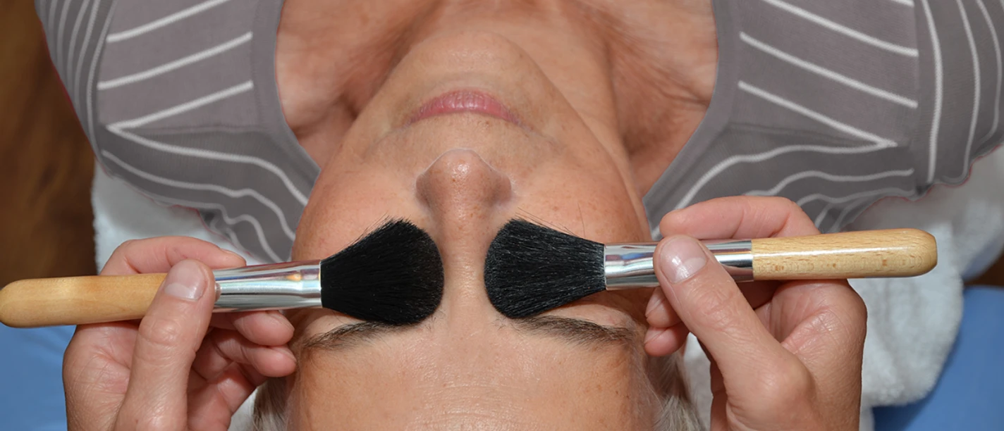 Entspannung bei Ines Bartz Eine Frau mit geschlossenen Augen genießt eine entspannende Behandlung mit zwei weichen Bürsten.