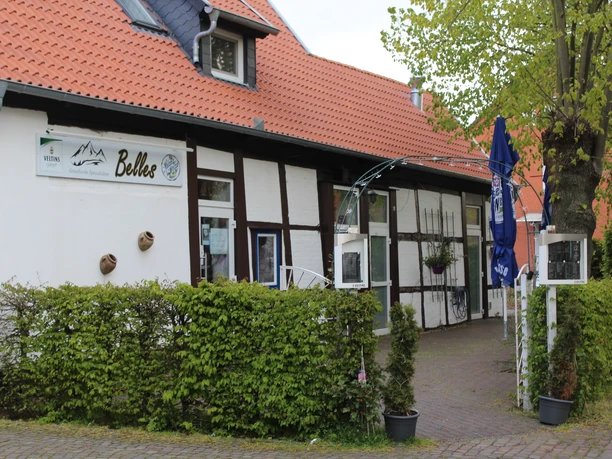 Historic half-timbered house with adjoining café and inviting garden, surrounded by a green hedge.