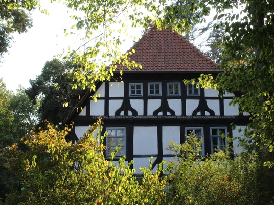 Alte Oberförsterei Uchte Altes Fachwerkgebäude mit rotem Ziegeldach, umgeben von Bäumen, künstlerisch eingefangen.