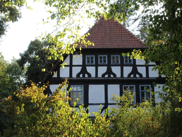 Alte Oberförsterei Uchte Altes Fachwerkgebäude mit rotem Ziegeldach, umgeben von Bäumen, künstlerisch eingefangen.