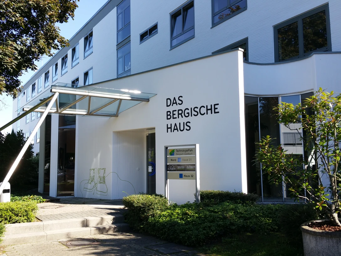 Das Bergische Haus.jpg Moderne Gebäudefront mit großem Schriftzug "Das Bergische Haus" und angrenzenden grünen Pflanzen.
