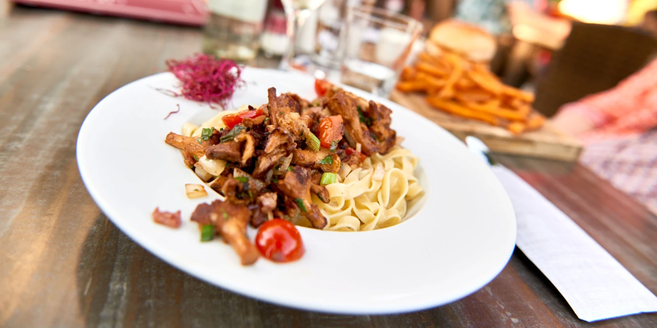 Franky's im Wasserbahnhof (2017), Mülheim an der Ruhr Ein vornehmer Teller mit einer leckeren Nudelpfanne, daneben ein Getränkeglas auf einem Holztisch.