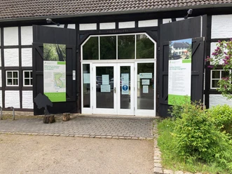 Forsthaus Steinhaus Eingang eines Fachwerkgebäudes mit weißen Wänden, großen Glastüren und informativen Schautafeln.