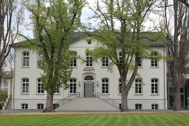 Besselsche Hof Ein weißes, zweistöckiges Gebäude mit symmetrischen Fenstern, umgeben von grünen Bäumen und Rasenflächen.