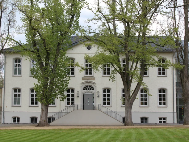 Besselsche Hof Ein weißes, zweistöckiges Gebäude mit symmetrischen Fenstern, umgeben von grünen Bäumen und Rasenflächen.