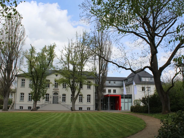 Besselscher Hof Der Besselsche Hof ist ein elegantes weißes Herrenhaus mit roten Akzenten, umgeben von Bäumen.