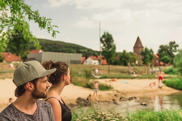 Emmerauenpark Lügde Zwei Personen stehen an einem Flussufer im Emmerauenpark Lügde, umgeben von grüner Natur.