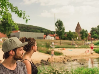 Emmerauenpark Lügde Zwei Personen stehen an einem Flussufer im Emmerauenpark Lügde, umgeben von grüner Natur.