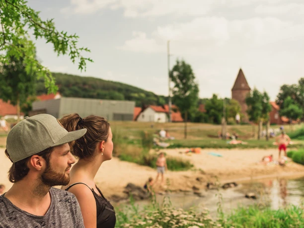 Emmerauenpark Lügde Zwei Personen stehen an einem Flussufer im Emmerauenpark Lügde, umgeben von grüner Natur.