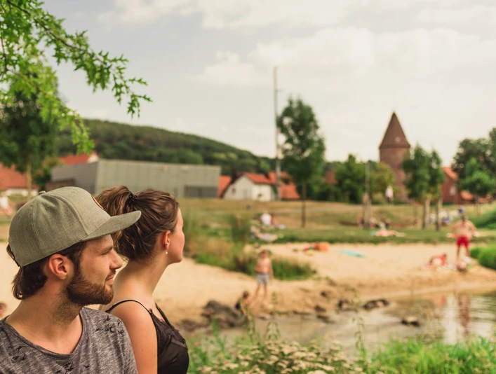 Emmerauenpark Lügde Zwei Personen stehen an einem Flussufer im Emmerauenpark Lügde, umgeben von grüner Natur.