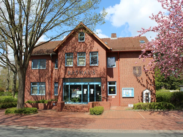 Das historische Rathaus Eystrup aus Backstein mit blühenden Bäumen flankiert den Eingangsbereich.