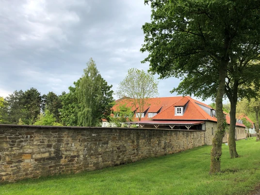 Gut Neuhof Petershagen Verwunschenes Gut Neuhof mit rotem Ziegeldach, umgeben von steinerner Mauer und saftigem Grün.