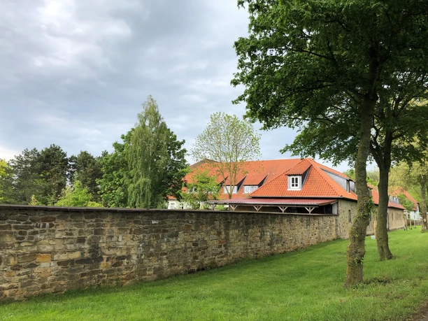 Gut Neuhof Petershagen Verwunschenes Gut Neuhof mit rotem Ziegeldach, umgeben von steinerner Mauer und saftigem Grün.