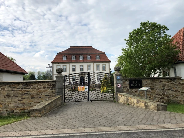 Gut Neuhof Petershagen Eingangstor mit Kopfsteinpflaster führt zu einem historischen, dreistöckigen Herrenhaus mit roten Dächern.