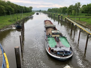 Frachtschiff durchquert die Schleuse Landesbergen auf der Weser, umgeben von grünen Ufern und Schiffen.