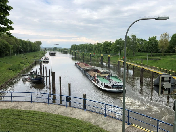 Schleuse Landesbergen mit Frachtschiff auf dem Kanal, umgeben von grüner Landschaft unter blauem Himmel.