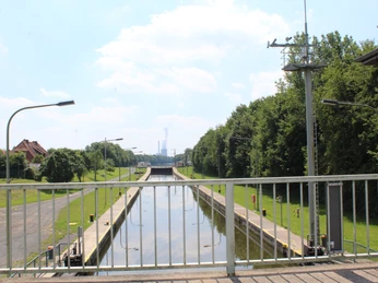 Schleuse Petershagen Ein Blick über eine Schleuse mit ruhigem Wasser, flankiert von grünen Bäumen und einem blauen Himmel.