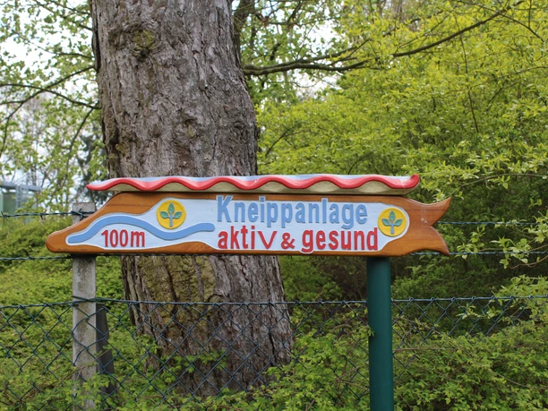 Kneippanlage Hoya Wegweiser zur Kneippanlage, umgeben von Bäumen und Pflanzen, weist in 100 Metern auf das Ziel hin.
