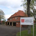 Stadtarchiv Petershagen Das Stadtarchiv Petershagen mit rotem Backsteingebäude und Bushaltestelle, umgeben von grünen Bäumen.