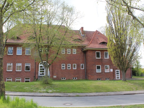 Stadtarchiv Petershagen Backsteingebäude mit roten Dachziegeln und mehreren Fenstern, umgeben von Bäumen und Rasen.