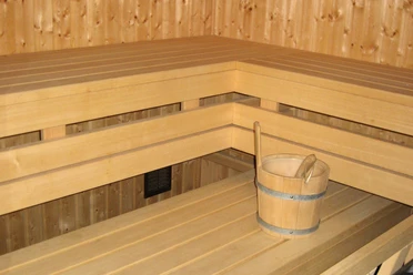 Helle Holzsauna mit mehreren Bänken und einem Holzeimer auf der unteren Bank in modernem Design.