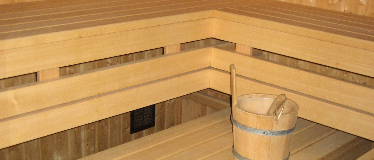 Helle Holzsauna mit mehreren Bänken und einem Holzeimer auf der unteren Bank in modernem Design.