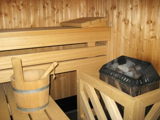 Sauna Holzverkleidete Sauna mit Holzbank, einer Kelle im Eimer und einem Ofen voller Sauna-Steine.