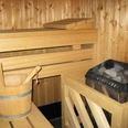 Sauna Holzverkleidete Sauna mit Holzbank, einer Kelle im Eimer und einem Ofen voller Sauna-Steine.