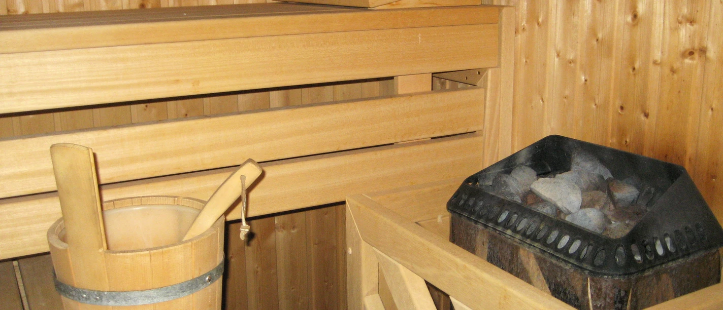 Sauna Holzverkleidete Sauna mit Holzbank, einer Kelle im Eimer und einem Ofen voller Sauna-Steine.