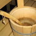 Ein hölzerner Saunakübel mit Wasser steht auf einer Holzbank neben einer Saunaaufguss-Kelle.