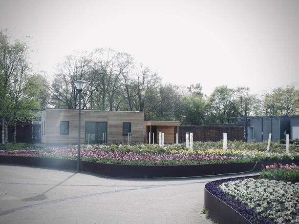 Eine moderne Holzhütte in einem farbenprächtigen Frühlingsgarten voller blühender Blumenbeete.