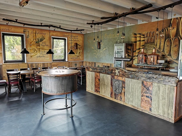 Rustikale Brauerei-Innenansicht mit Holztischen, Wandmalereien und Braukessel in einer gemütlichen Atmosphäre.