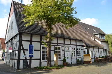 Café zur Linde Langenberg 1.JPG Fachwerkhaus mit Baum im Vordergrund, blauem Schild und gemütlicher Sitzgelegenheit außen.