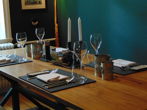 Restaurant Gedeckter Holztisch im Restaurant mit grauen Platzsets, Gläsern, Kerzen und Dekoration.