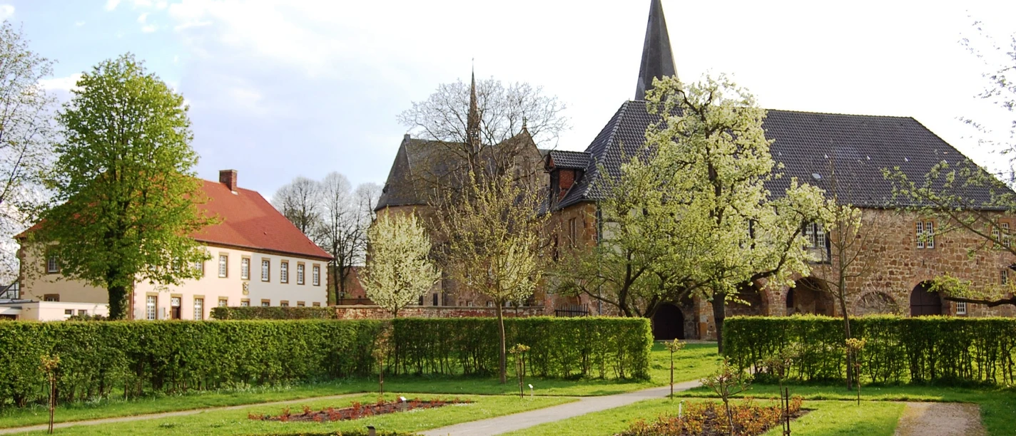 Klostergarten_Herzebrock Historisches Gebäude mit Fachwerk und markantem Kirchturm, umgeben von blühendem Garten und Wegen.