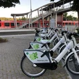 Mobilstation Bergisches e-Bike Bahnhof Overath Fahrräder von "Bergisches e-Bike" an einem Bahnhof, mit rotem Zug im Hintergrund.