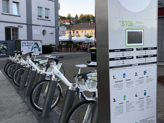 Mobilstation Bergisches e-Bike Bahnhof Overath Eine E-Bike-Station in einem städtischen Umfeld mit mehreren bereitstehenden Fahrrädern.