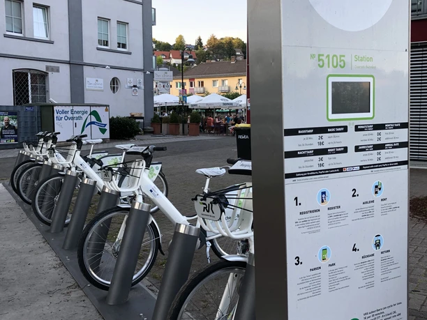 Mobilstation Bergisches e-Bike Bahnhof Overath Eine E-Bike-Station in einem städtischen Umfeld mit mehreren bereitstehenden Fahrrädern.