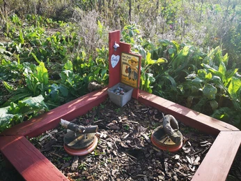 Hummelwiese Hampenhausen Holzskulpturen in quadratischer Holzrahmung, umgeben von grünem Pflanzenbewuchs mit Vogeltränke.
