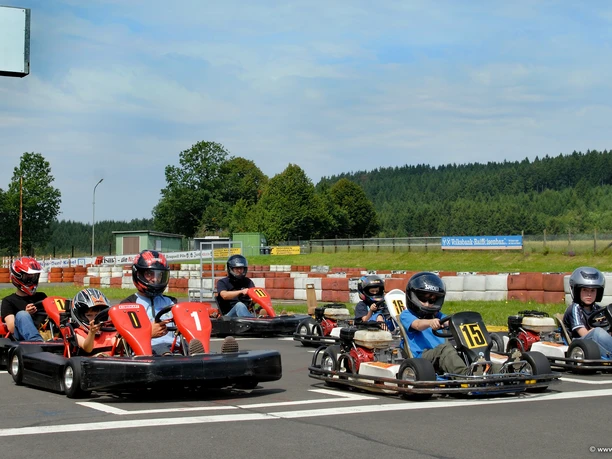 Kartbahn Menschen fahren auf einer Outdoor-Kartbahn in Go-Karts; umgeben von Natur und Bäumen.