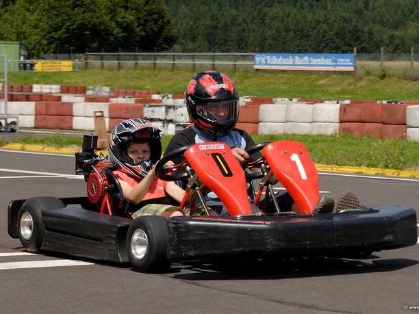 Kartbahn Zwei Personen fahren in einem roten Doppelsitzer-Gokart auf einer asphaltierten Kartbahn.