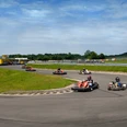 Kartbahn Eine Gruppe von Personen fährt in Go-Karts auf einer kurvenreichen Outdoor-Strecke bei sonnigem Wetter.