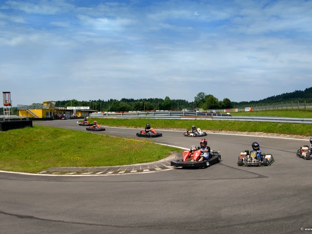 Kartbahn Eine Gruppe von Personen fährt in Go-Karts auf einer kurvenreichen Outdoor-Strecke bei sonnigem Wetter.